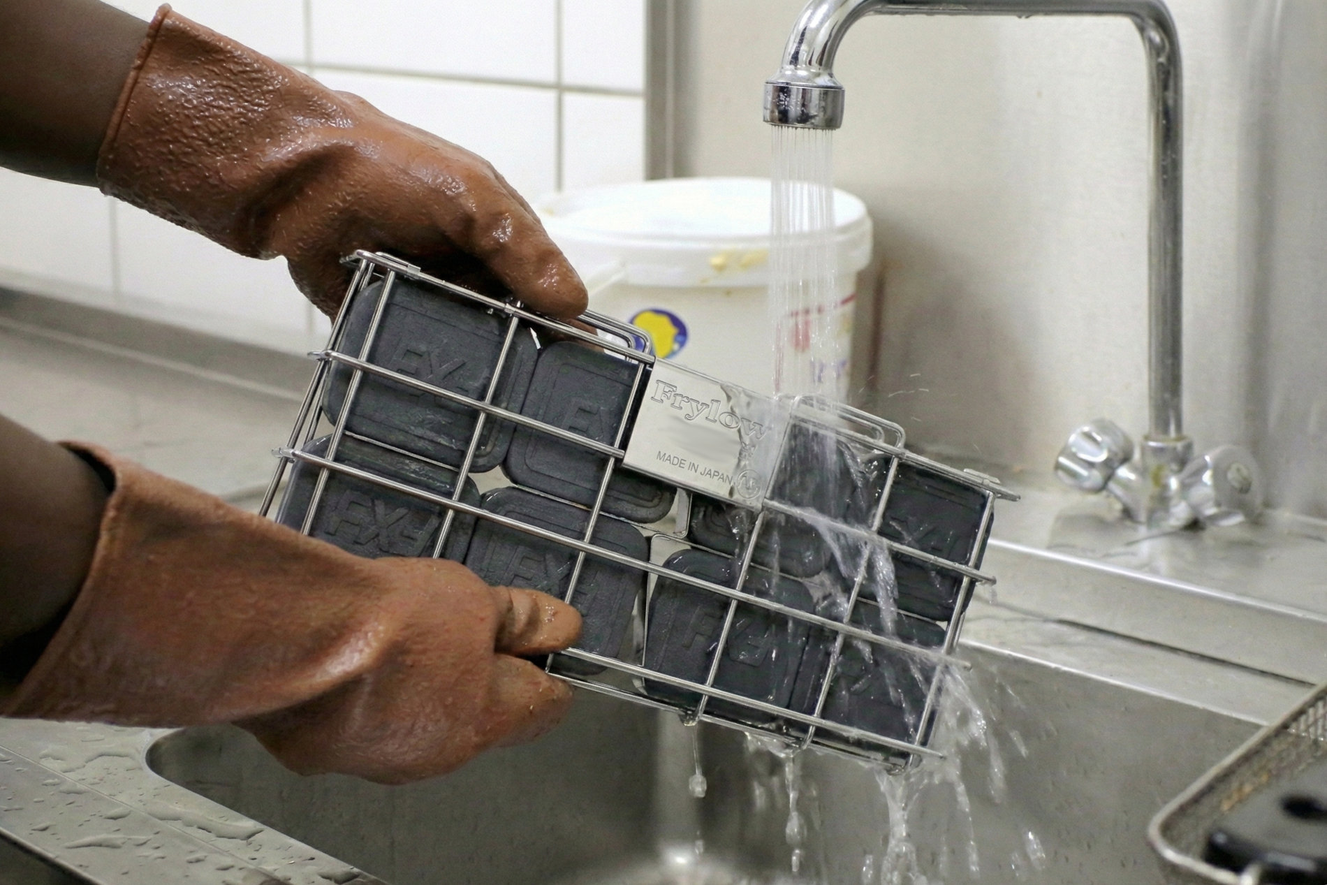 A chef rinses Frylow under hot water as part of the Frylow maintenance and cleaning guide.